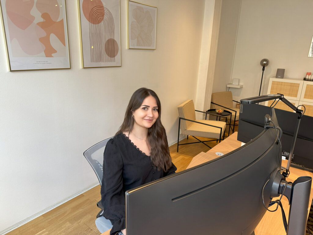 En kvinna som sitter bakom en stor datorskärm på kontoret.